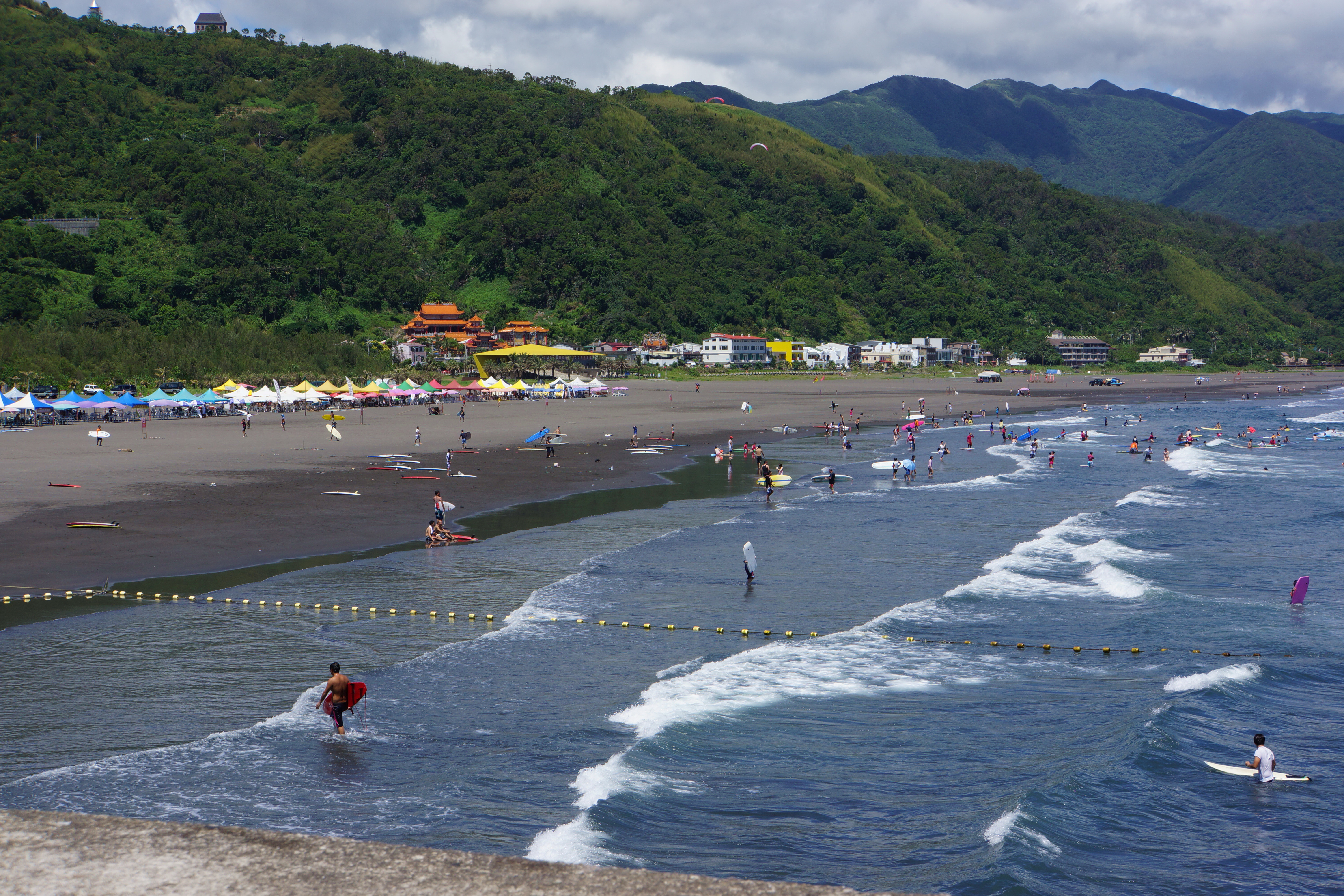 宜蘭頭城外澳海灘，海浪沿著黑色沙岸推進，遠處是翠綠山坡
